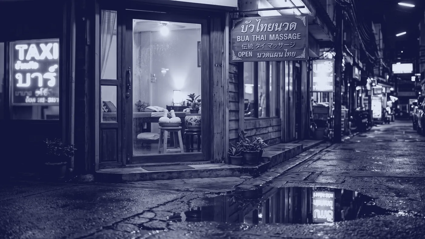 The shop doorway at night on Soi 24, one lamp lit inside and a basket of herbal compresses on a wooden stool.